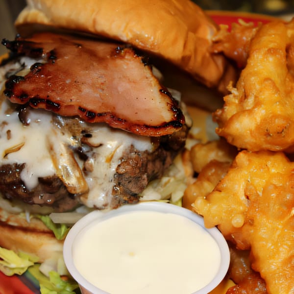 Abby Lane Gourmet Burger with melted cheese, bacon, lettuce, and a side of fried onion rings and dipping sauce.
