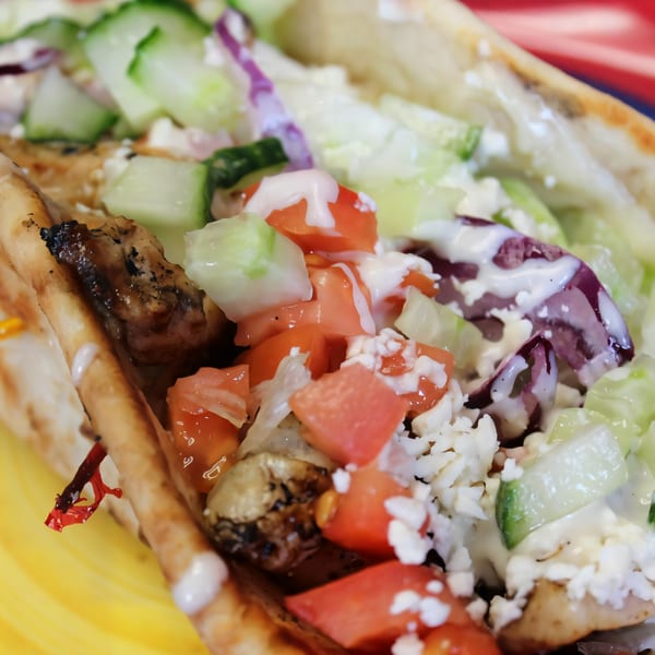 Close-up of a gyro with grilled chicken, diced tomatoes, cucumbers, red onions, feta, and white sauce.