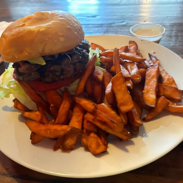 Abby Lane Gourmet Burger with lettuce, tomato, and mushrooms, served with a side of sweet potato fries.