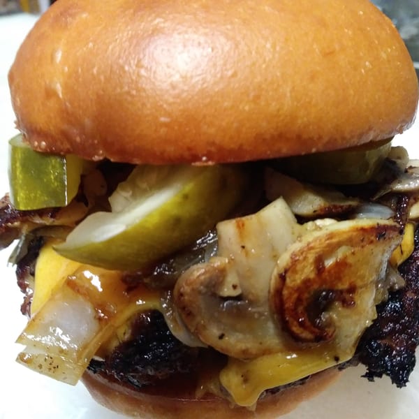 Close-up of an Abby Lane burger with melted cheese, grilled onions, mushrooms, and pickles.
