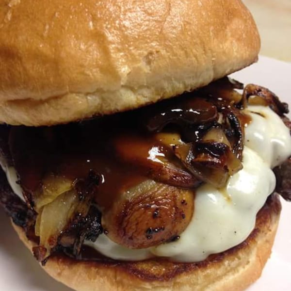 Abby Lane Gourmet Burger with melted cheese, caramelized onions, mushrooms, and gravy on a bun.